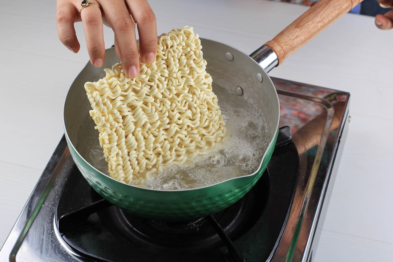 mão colocando macarrão instantâneo em uma panela com água fervendo